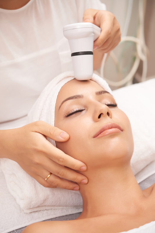 Modern beautician carrying out spa skincare procedure with special electric device